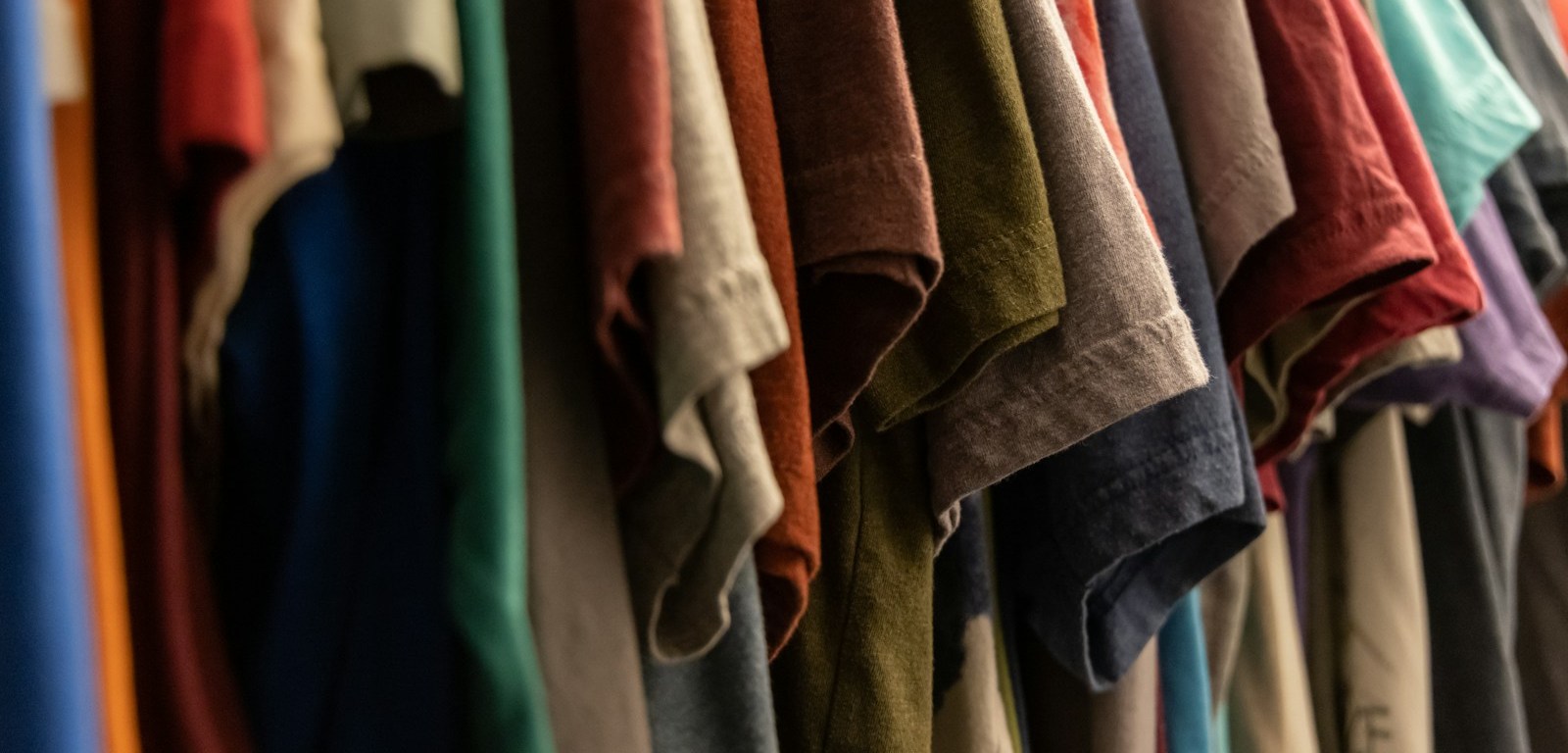 Camisetas de colores colgadas en perchas dentro de un armario