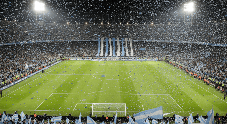 Estadio de fútbol lleno de noche con banderas celestes y blancas y papel picado