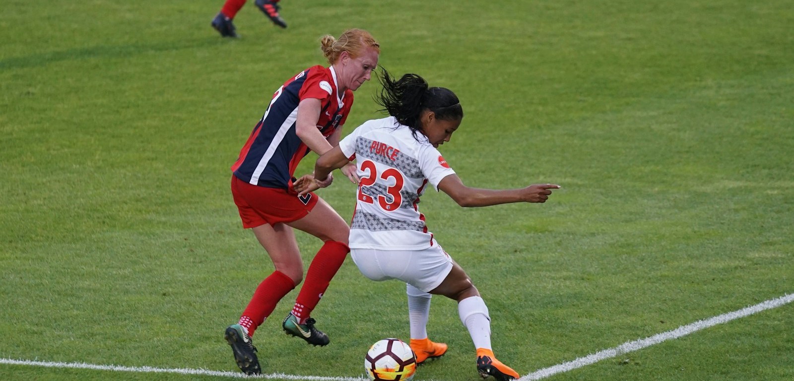 Dos jugadoras de fútbol disputan el balón en una cancha de césped