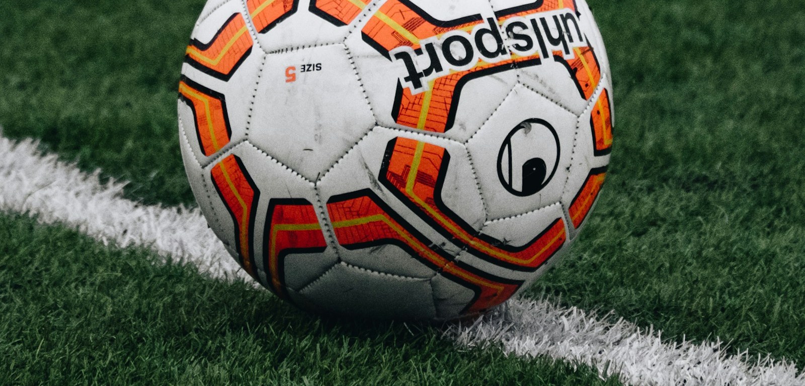 Un balón de fútbol sobre el césped junto a una línea blanca de la cancha