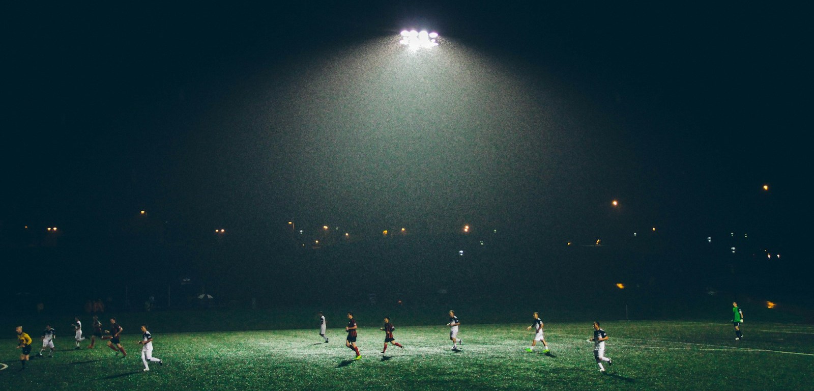 Partido de fútbol nocturno en una cancha de césped iluminada por reflectores