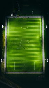 Vista aérea de una cancha de fútbol iluminada por reflectores de noche
