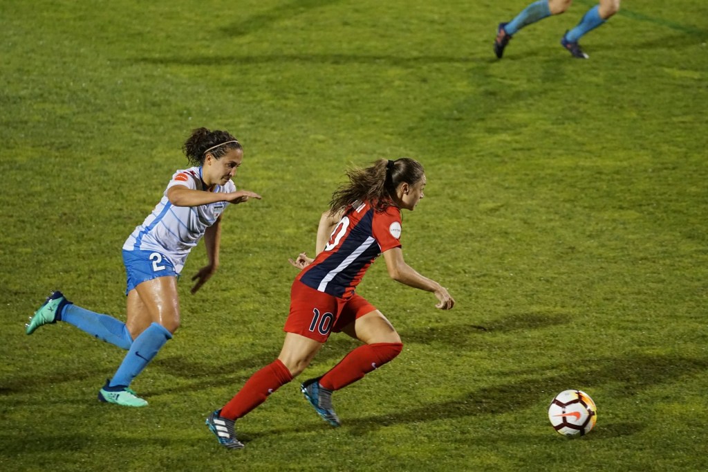 Dos jugadoras de fútbol disputan la pelota en una cancha de césped