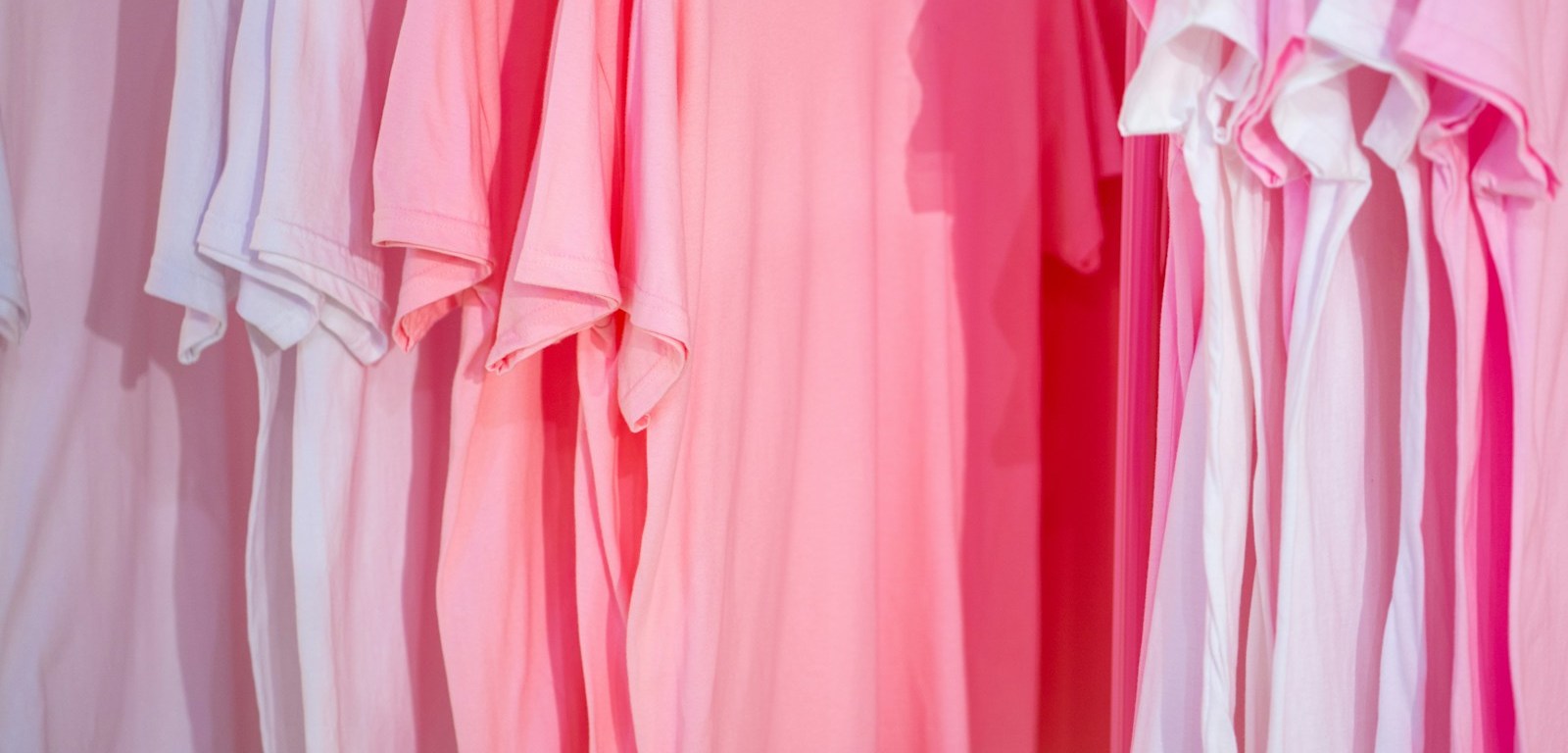 Camisetas lisas en tonos rosa y blanco colgadas en perchas