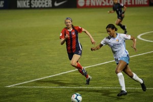 Una jugadora de fútbol conduce la pelota en una cancha de césped