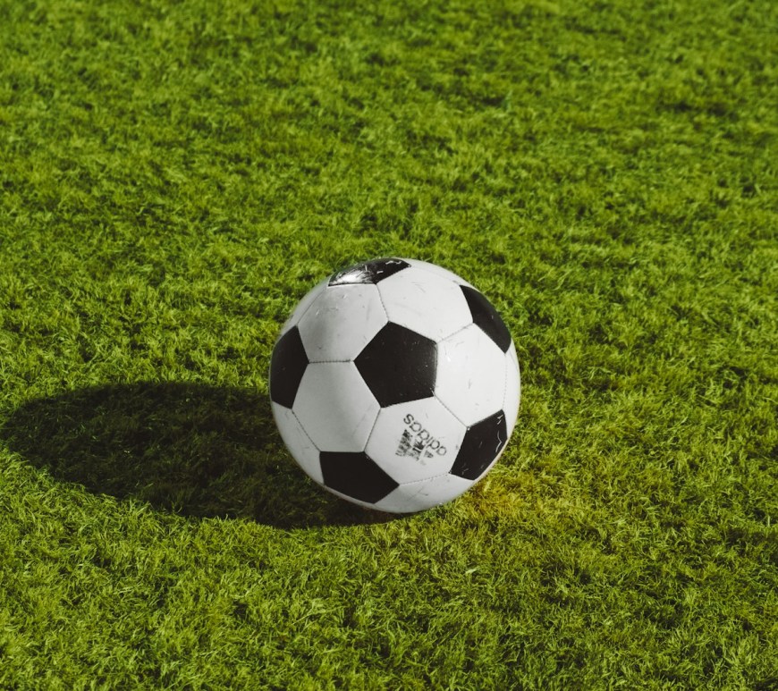 Balón de fútbol blanco y negro apoyado sobre el césped de una cancha