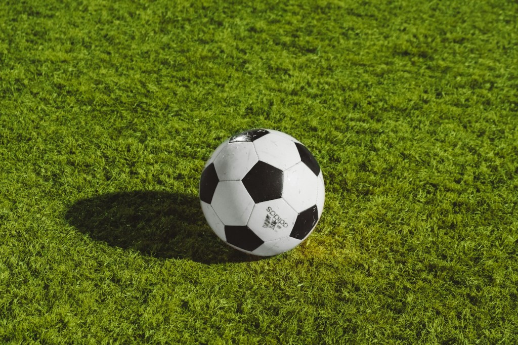 Balón de fútbol blanco y negro apoyado sobre el césped de una cancha
