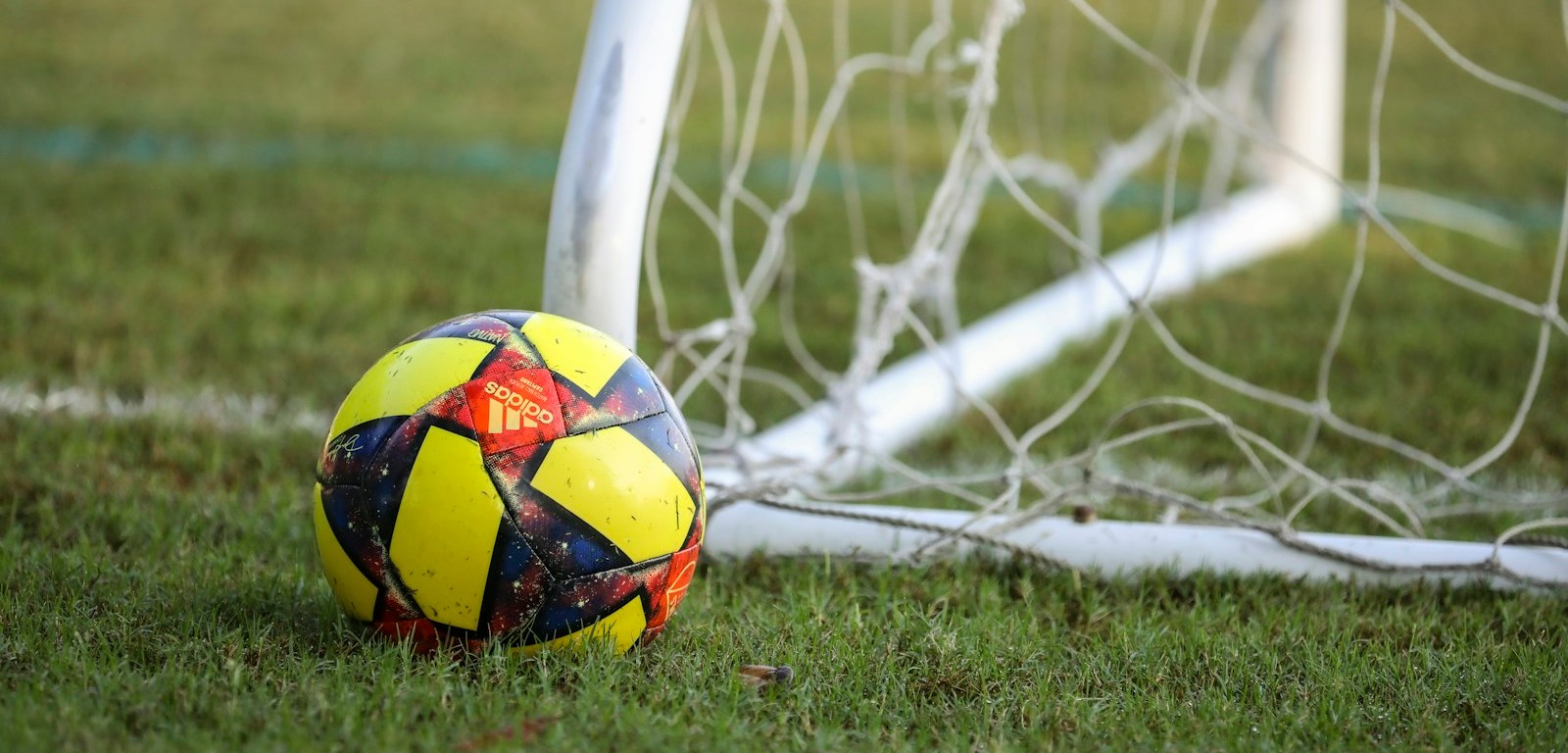 Balón de fútbol rojo, azul y amarillo sobre el césped frente a un arco