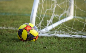 Balón de fútbol rojo, azul y amarillo sobre el césped frente a un arco