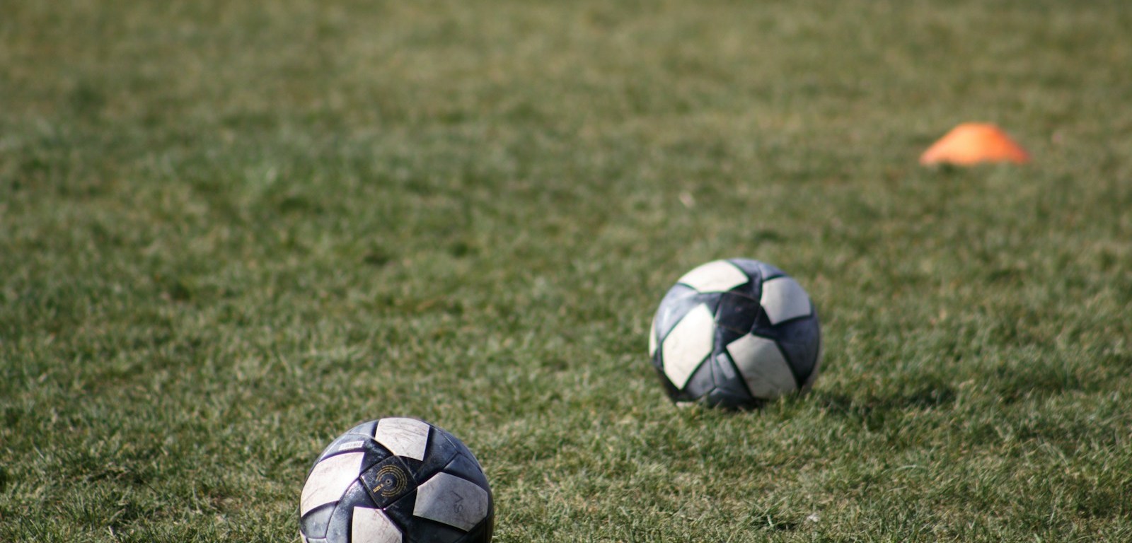 Dos balones de fútbol sobre el césped de una cancha de entrenamiento