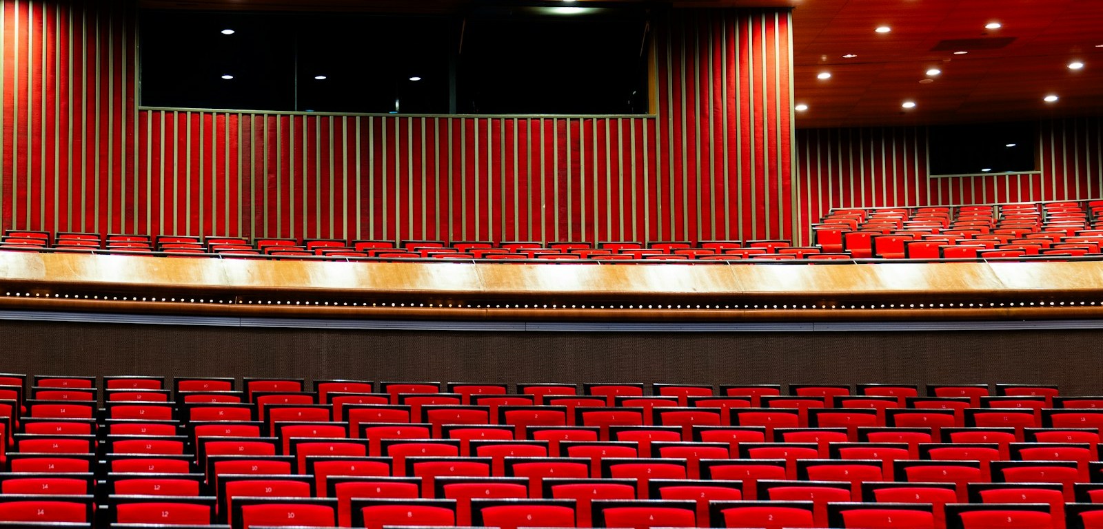 Auditorio vacío con butacas rojas, palcos y un escenario iluminado