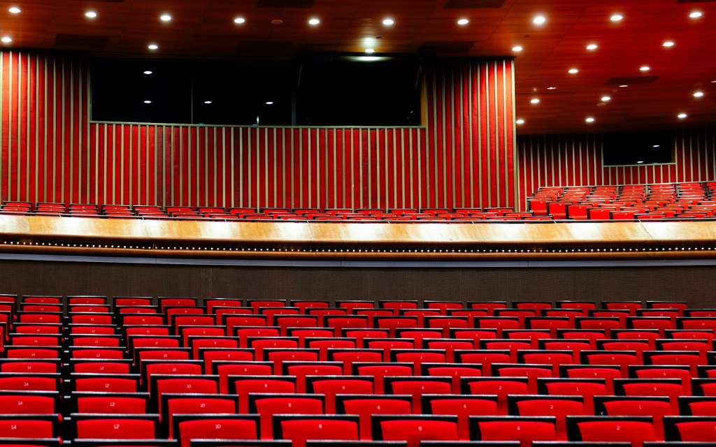 Auditorio vacío con butacas rojas, palcos y un escenario iluminado