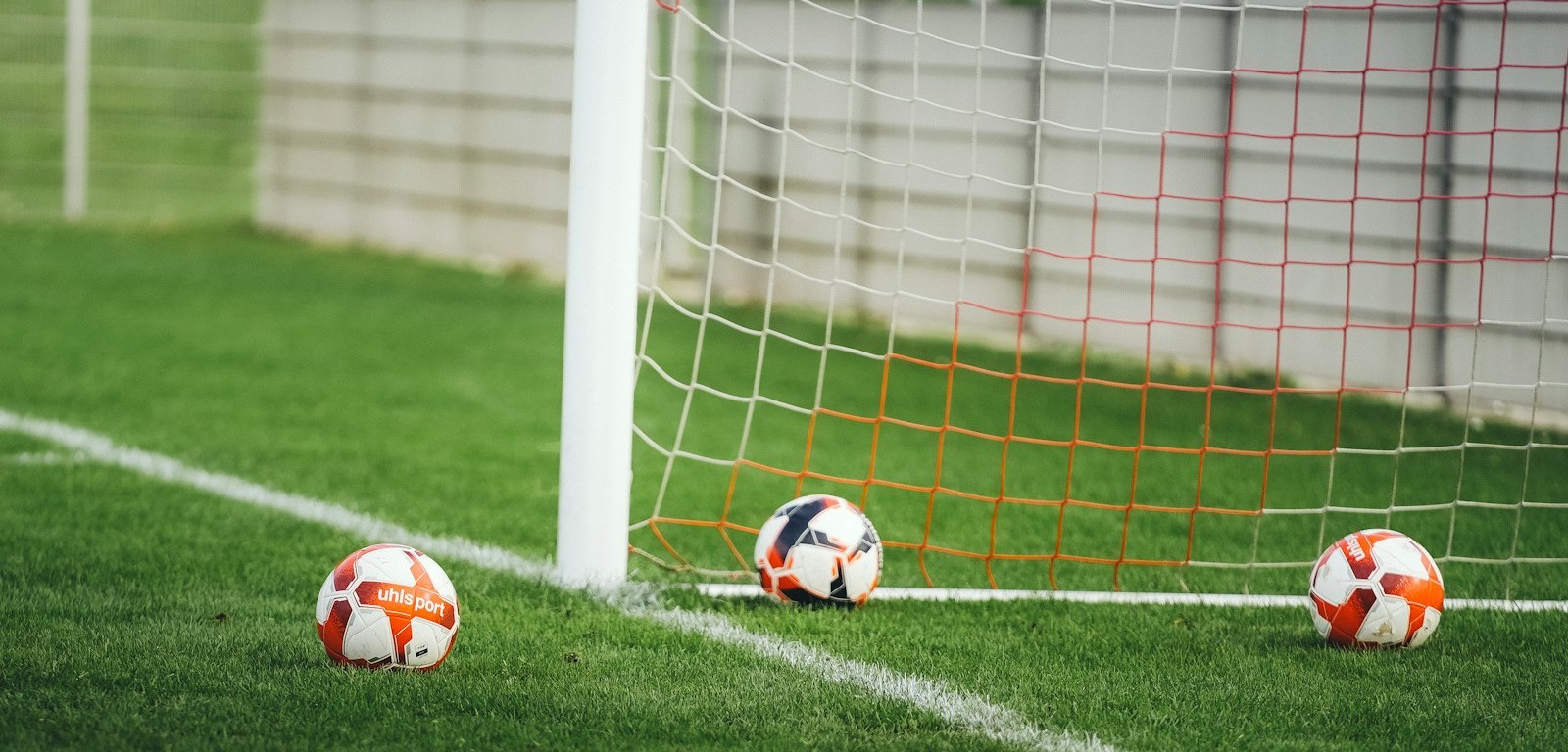 Tres balones de fútbol sobre el césped junto a la red de un arco