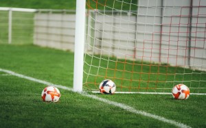Tres balones de fútbol sobre el césped junto a la red de un arco