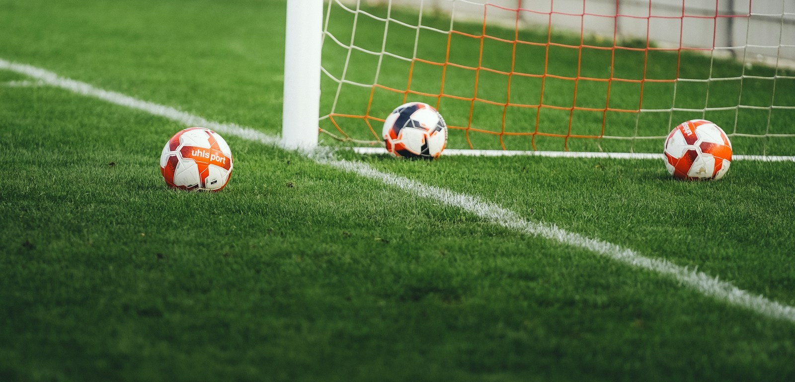 Tres balones de fútbol sobre el césped cerca de la red de un arco
