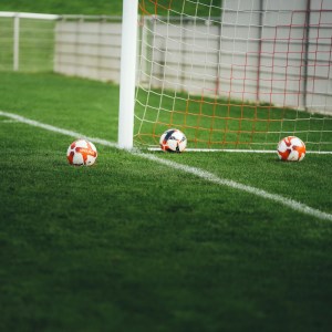 Tres balones de fútbol sobre el césped cerca de la red de un arco